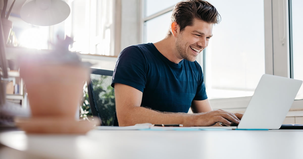 Smiling man sitting at a table using a laptop