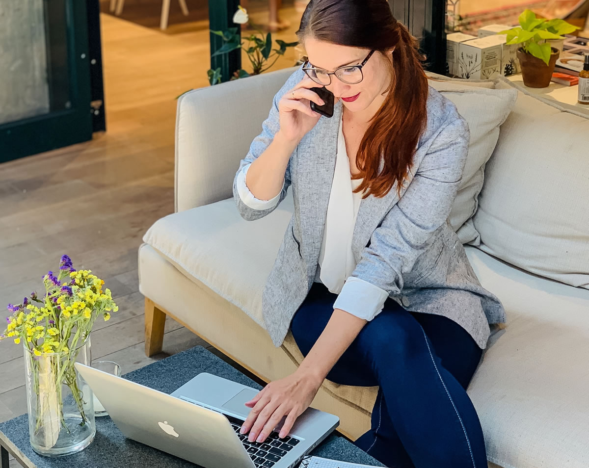 Businesswoman on mobile phone sitting on couch in front of coffee table with open laptop