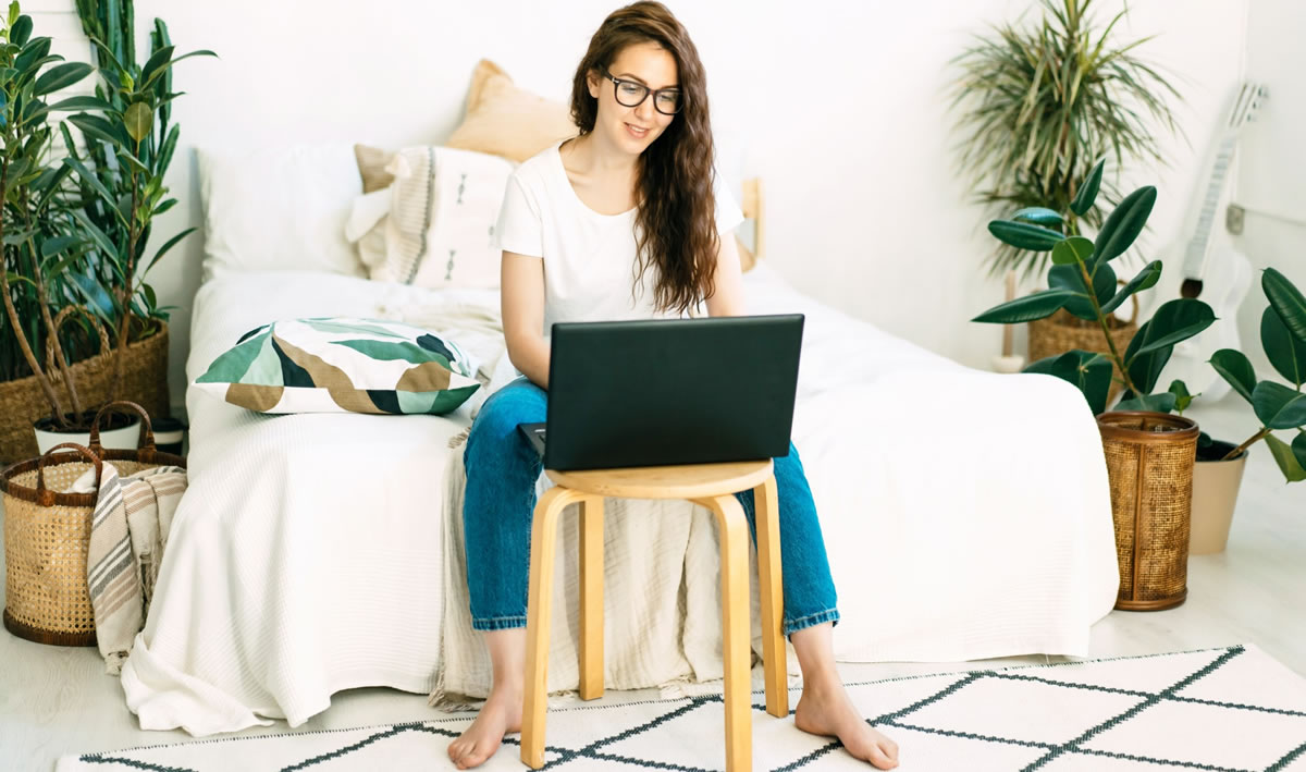 Woman writing on laptop, sitting at a table in her bedroom