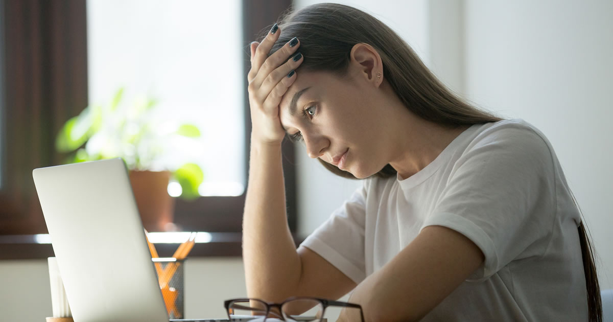 Woman with her forehead resting in her hand staring at a laptop