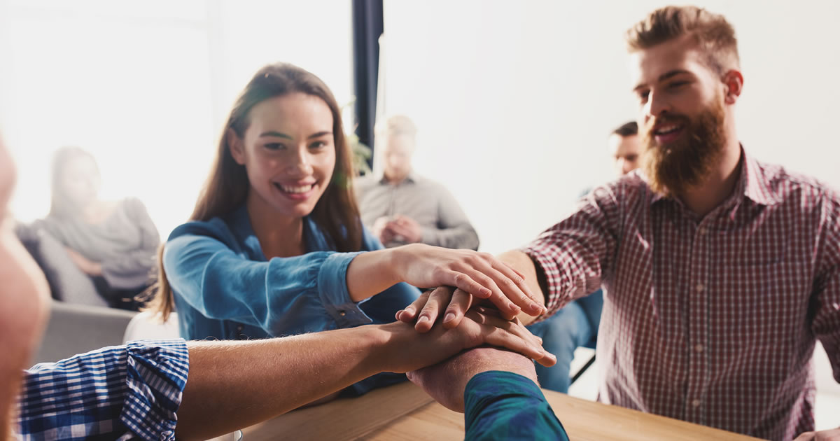 Grupo de pessoas sorridentes com as mãos juntas no meio do grupo