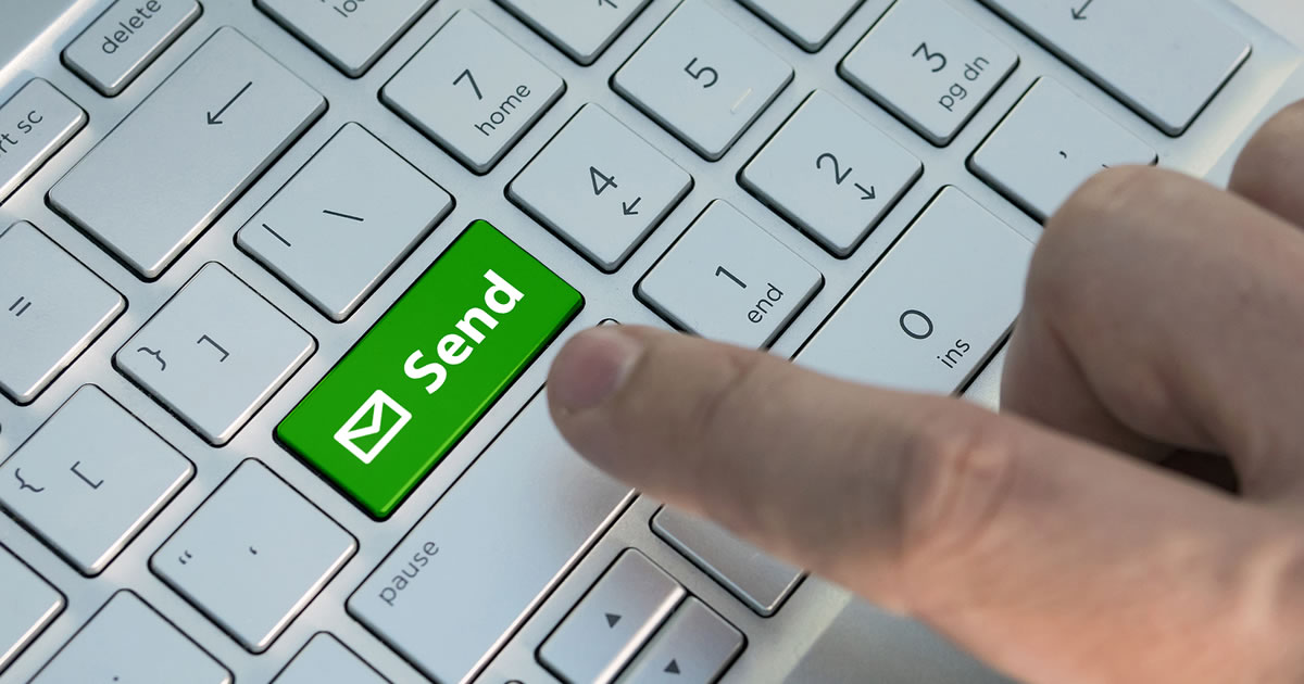 Email send button on the computer keyboard. A male finger presses a color email send button on a silver keyboard of a laptop