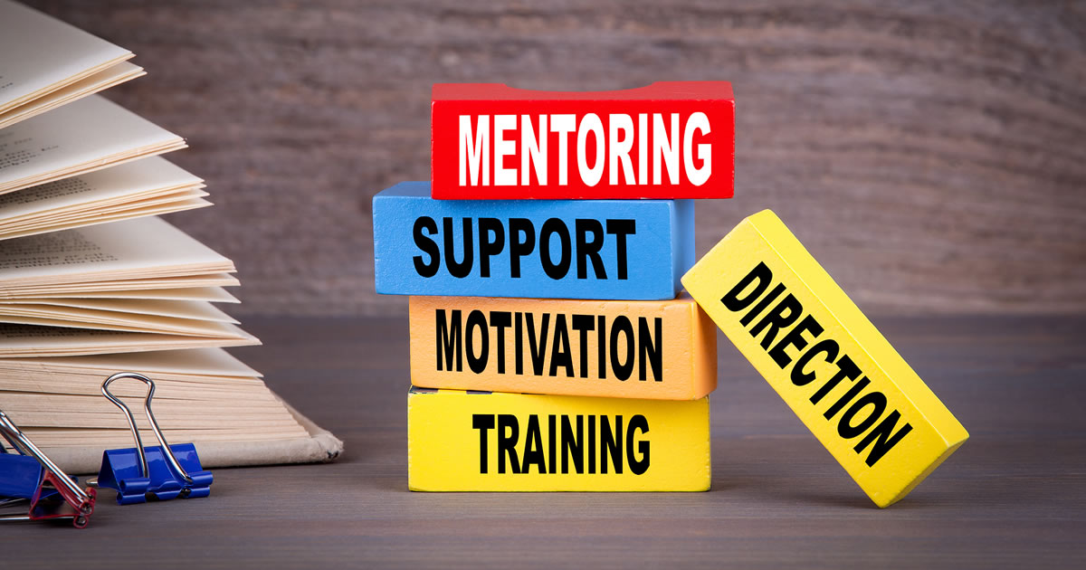 Different color wooden blocks labeled mentoring, support, training, motivation, and direction stacked on the table