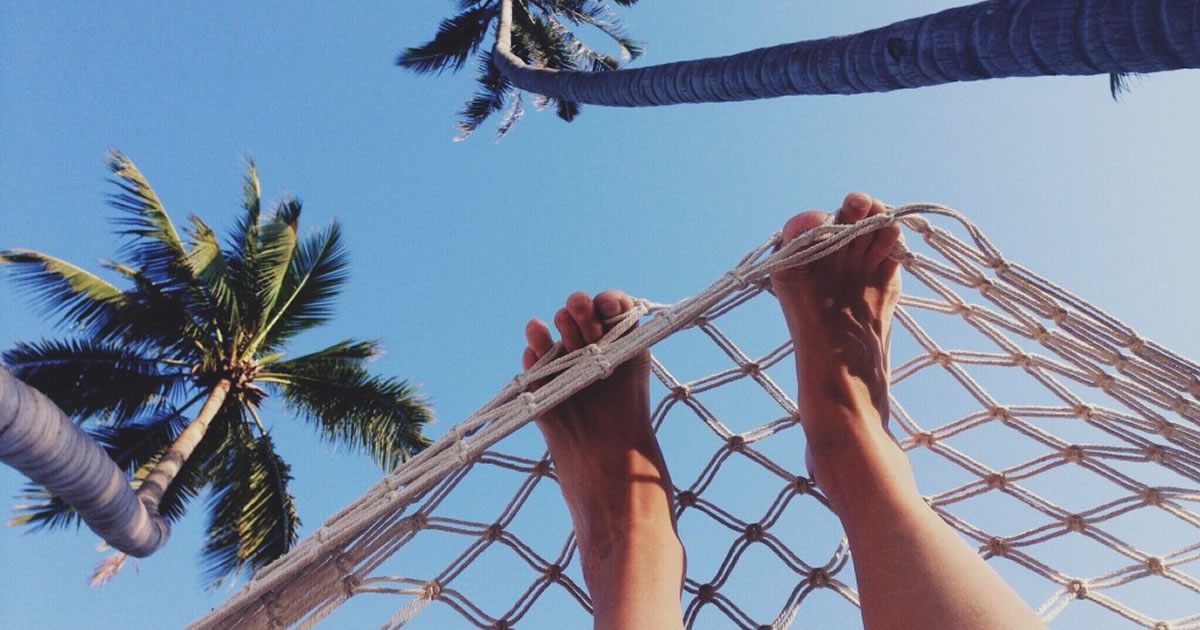 Person in hammock on beach with palm trees, only sandy bare feet showing