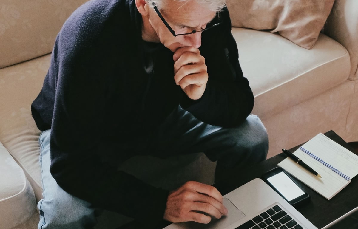 Man sitting on edge of couch, writing on laptop at coffee table