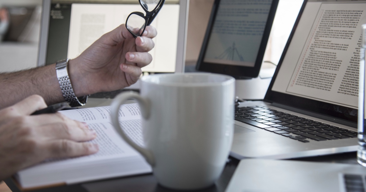 Man holding glasses reading next to a laptop