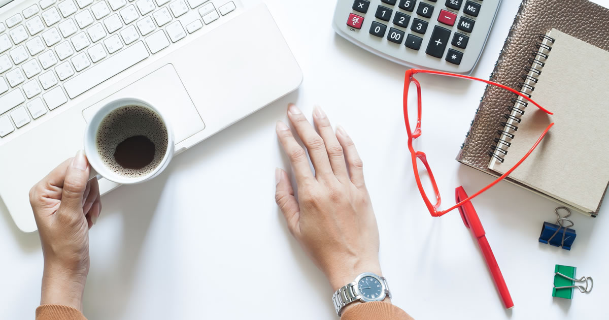 Writer holding a cup of coffee, at desk with laptop and calculator