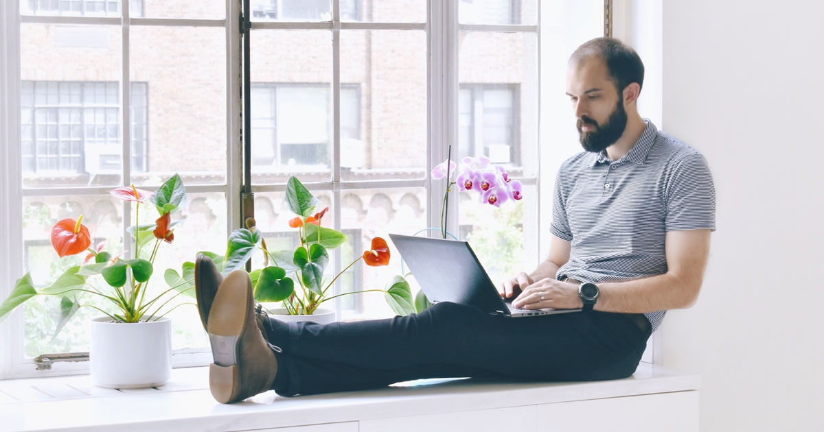 Man typing on laptop while sitting on window seat