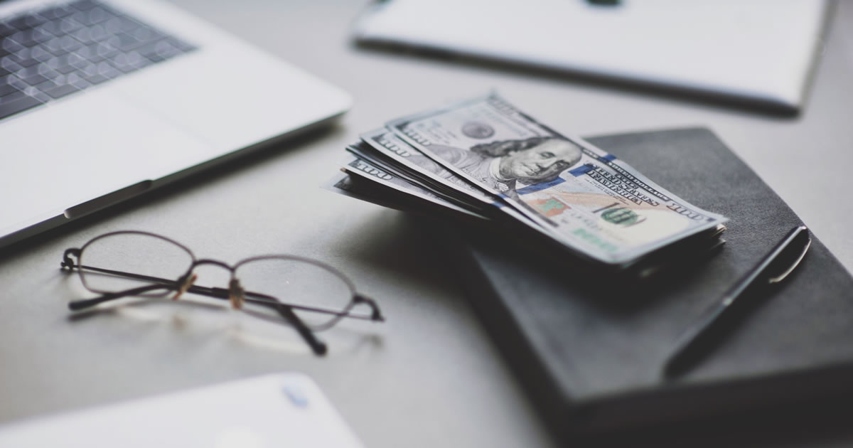 Laptop computer with stack of money and smartphone on a desk