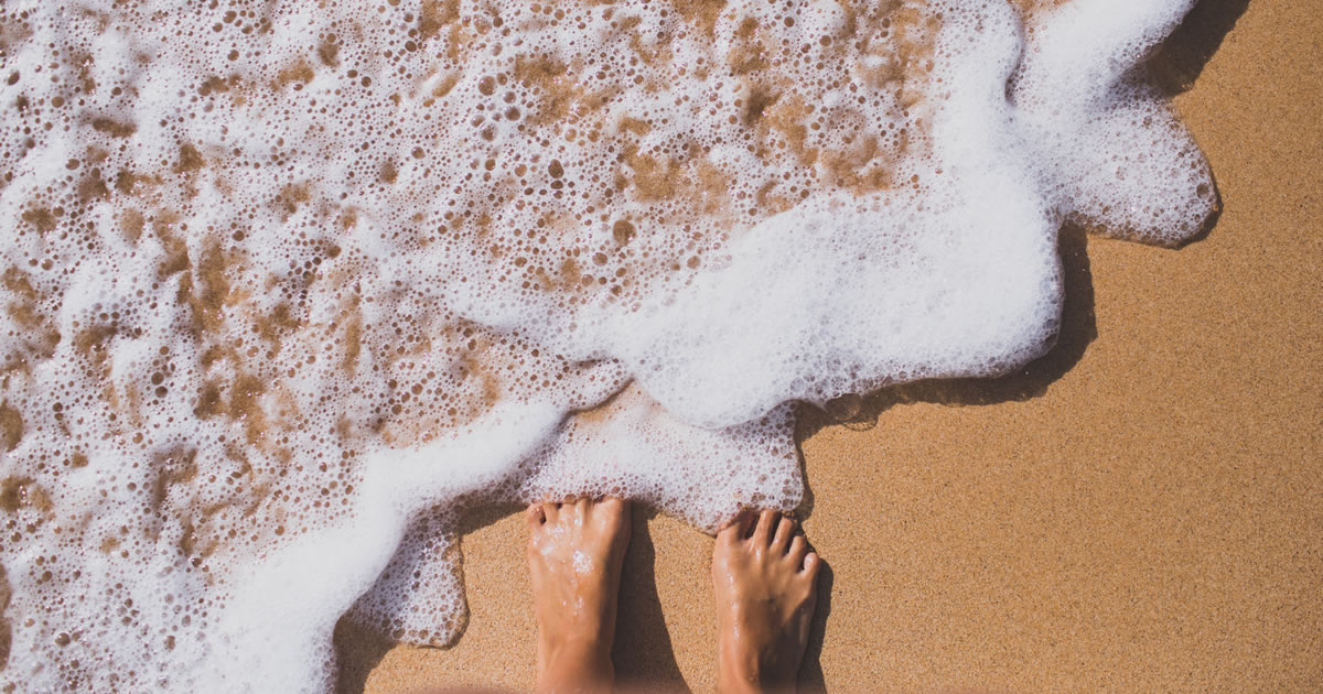 Seafoam partially covering bare feet on a sandy beach