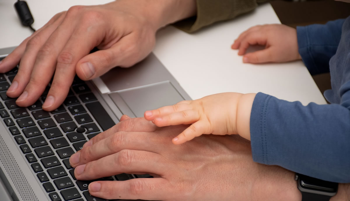 Father writing on laptop with baby's hands on top of his