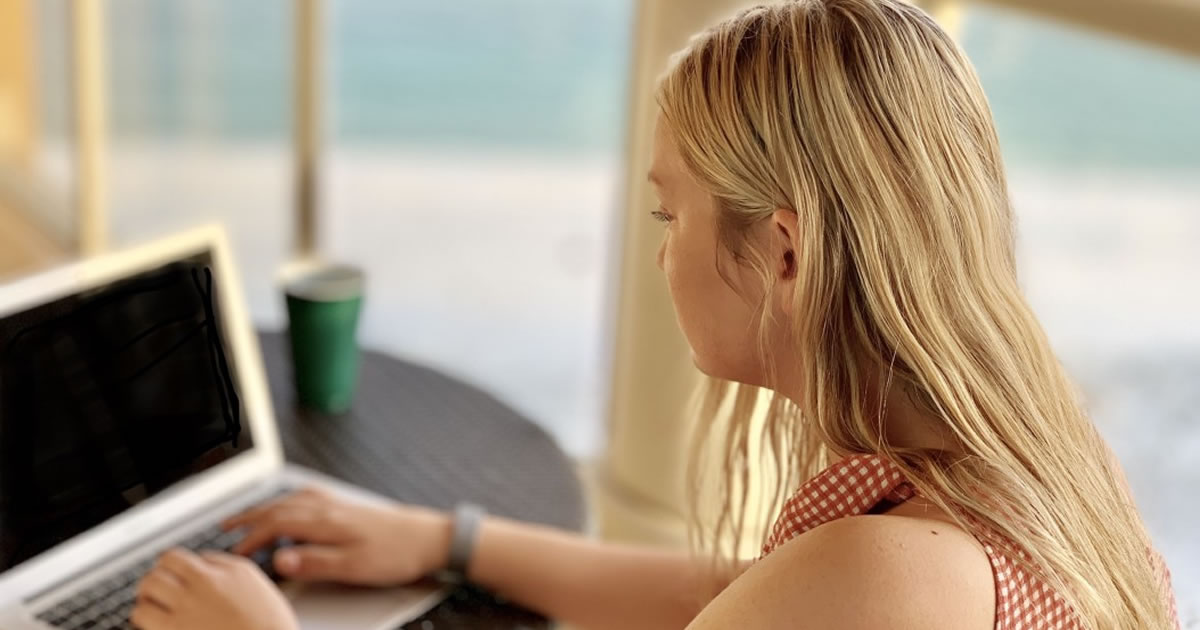 Young woman writing on laptop on balcony at beach