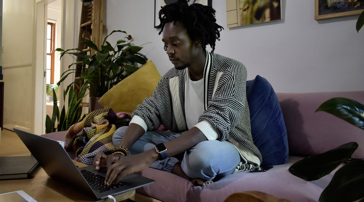 Man sitting on couch at home using laptop on coffee table