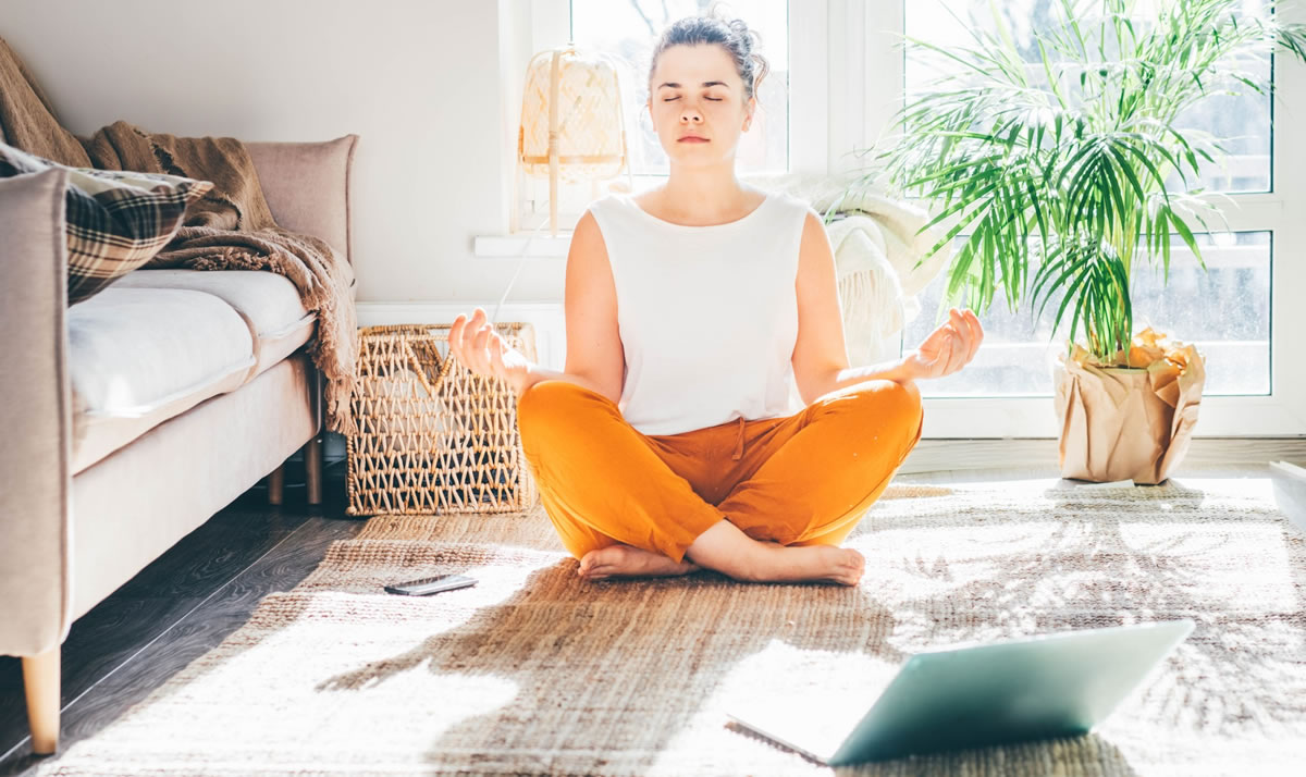 Woman sitting cross-legged on the floor meditating with laptop