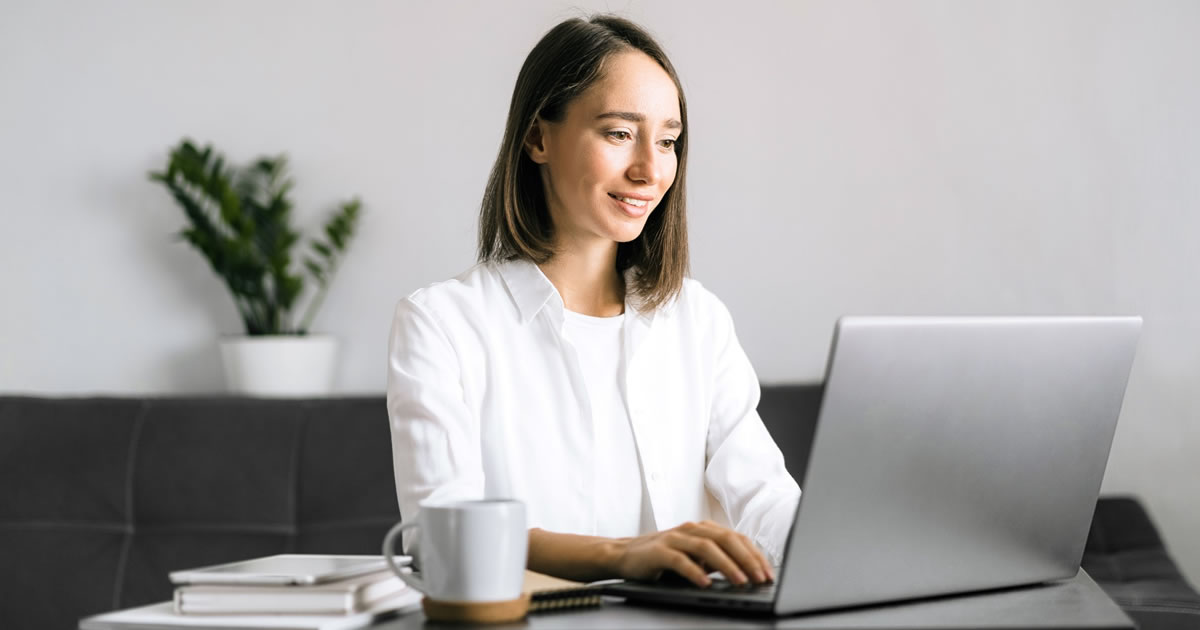 Young woman sitting at a desk, writing on laptop at her home office