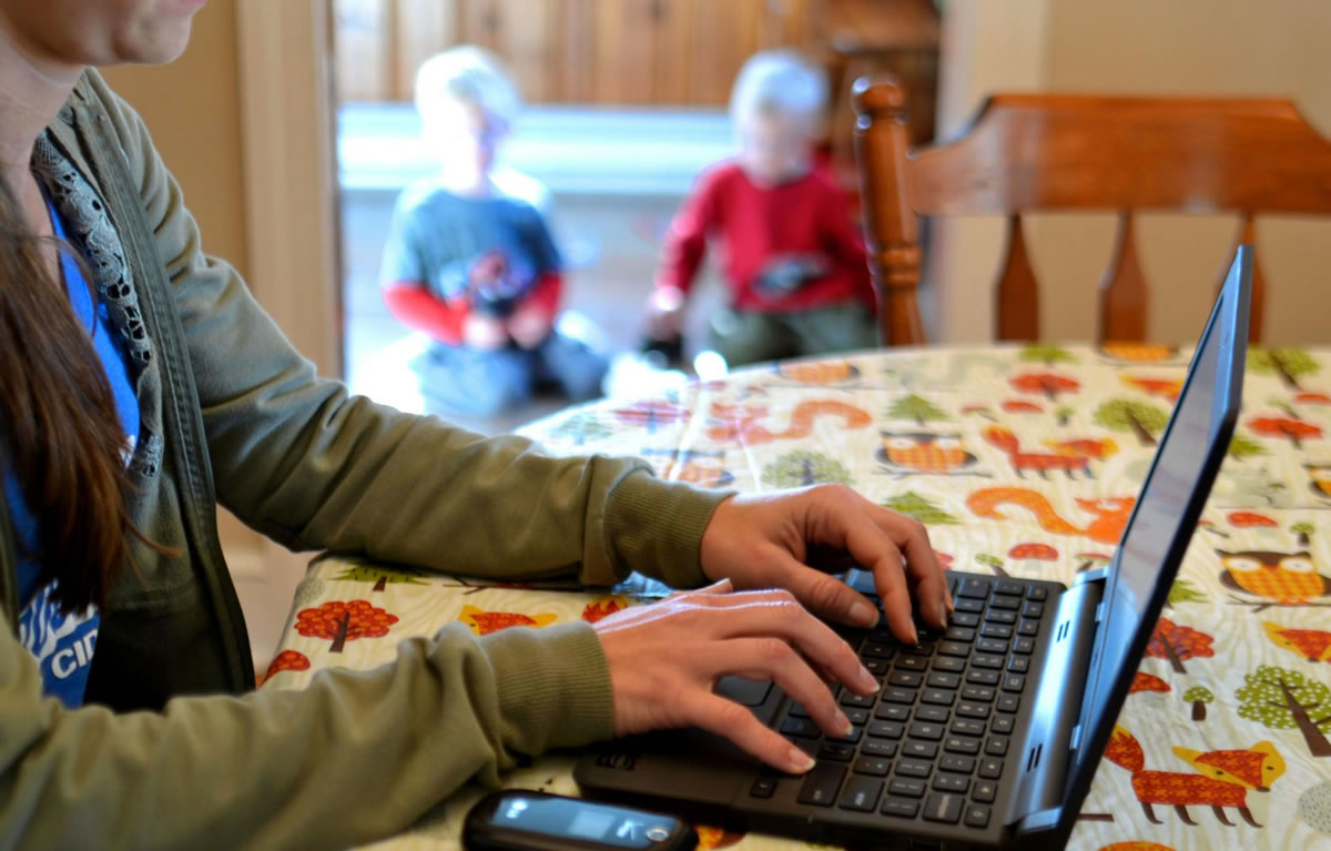 Mother writing on computer at home while her boys play in background