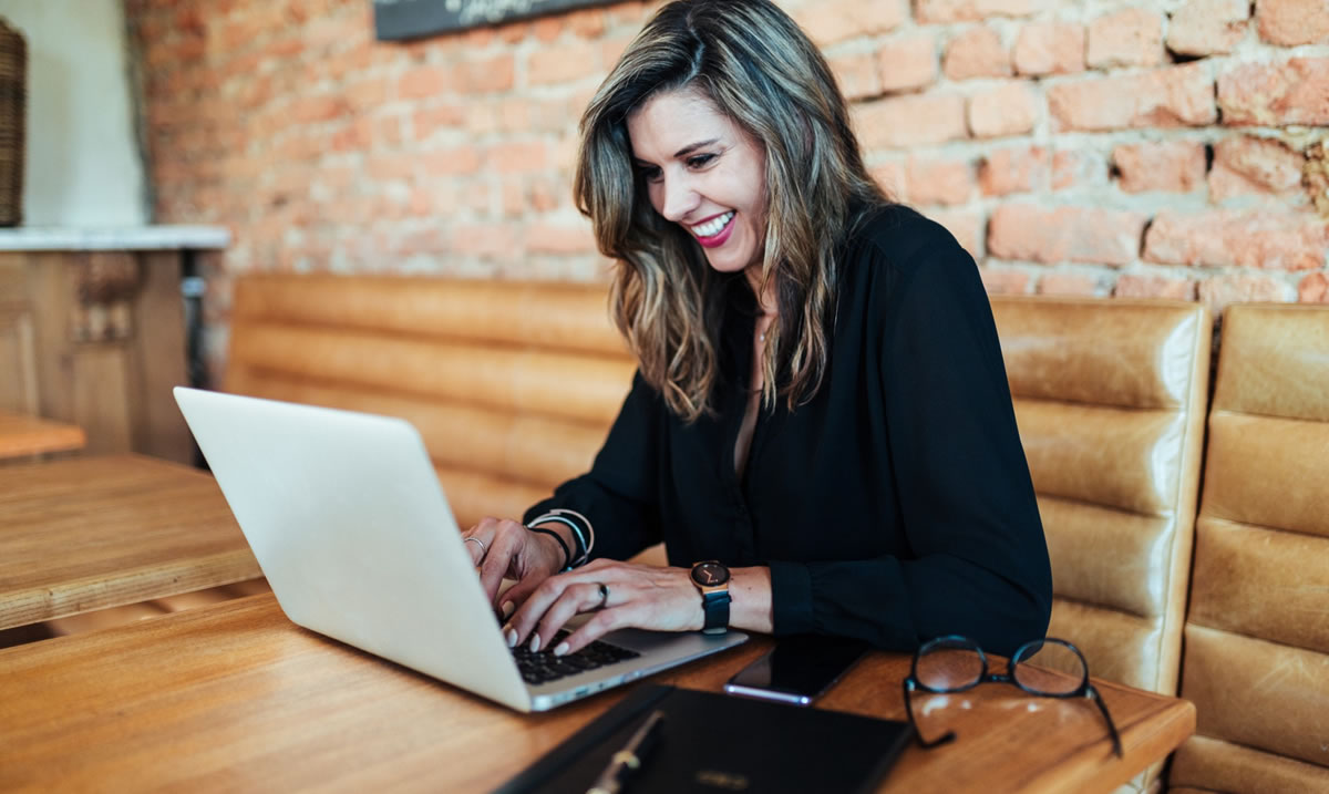 Mulher de negócios sorridente escrevendo no laptop em uma mesa