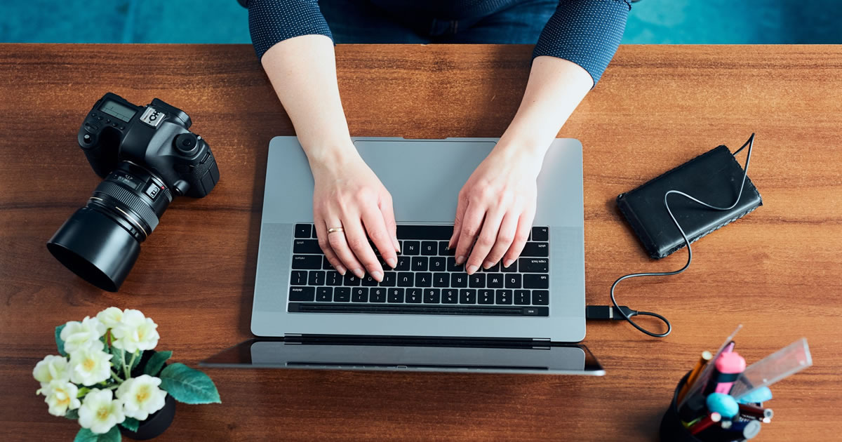 Female photographer and writer working on laptop at desk