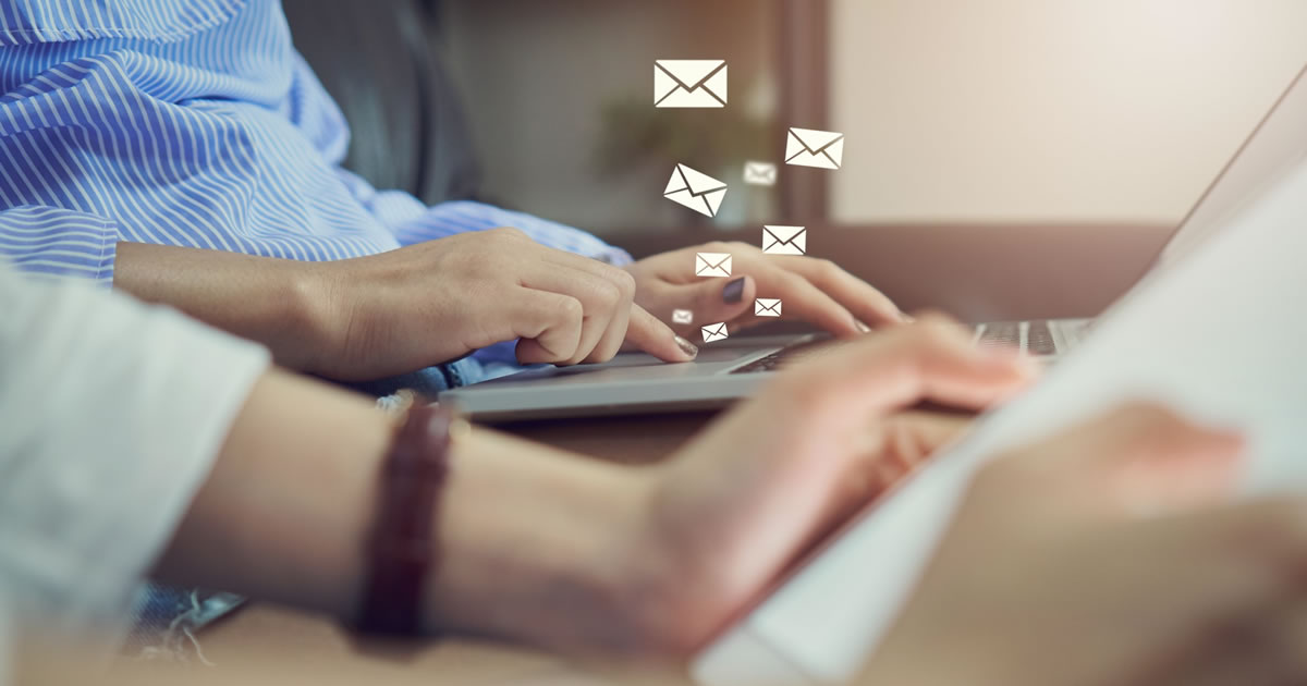 Woman writing on laptop with email icons floating above it