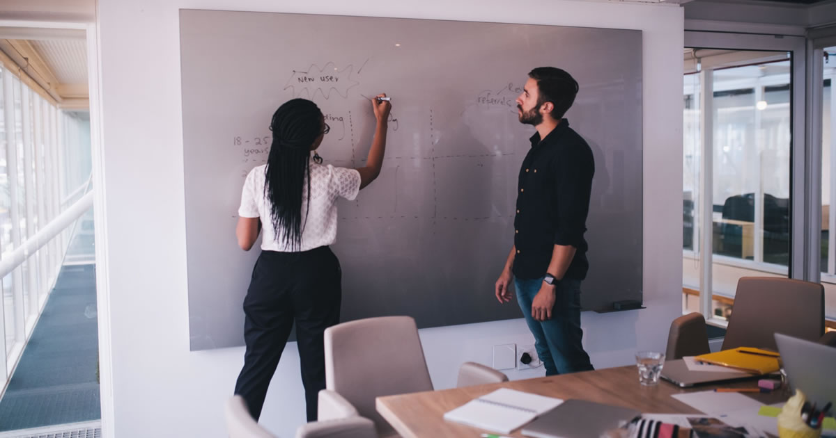 Colleagues using large dry erase board on wall