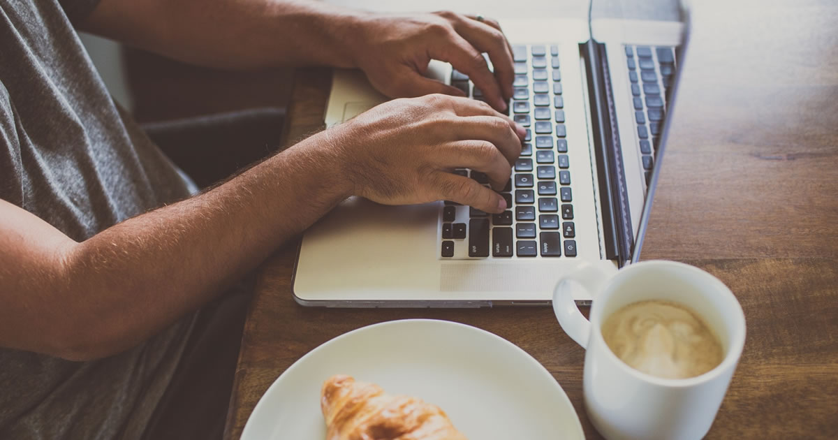 Man writing on laptop at table with coffee and croissant