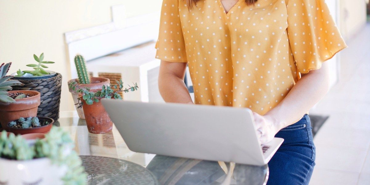 Woman in yellow shirt writing on laptop computer at table