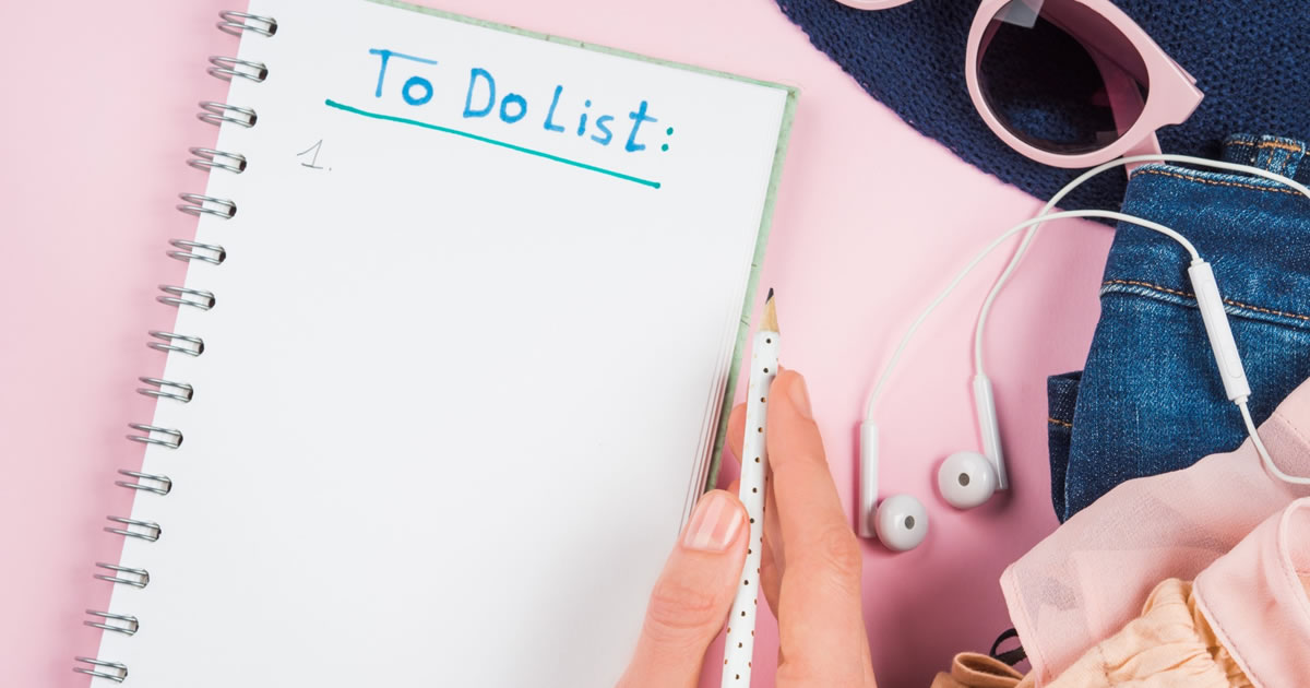 Closeup of woman's hand with pencil and to do list next to sunglasses and earphones