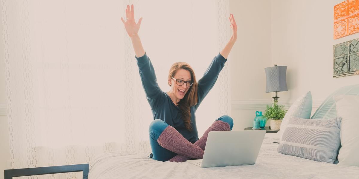 Happy writer with laptop raising her arms in celebration