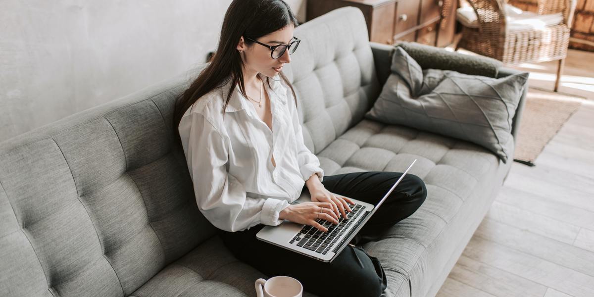 Young business woman writing on laptop sitting comfortably on couch