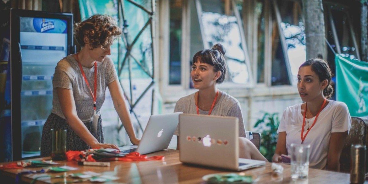 Three female coworkers discussing plans and working on laptops