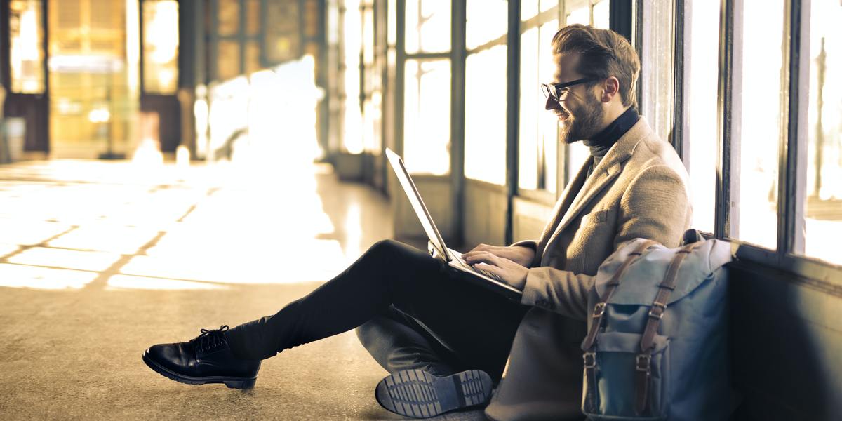 Happy man writing on laptop sitting on the floor