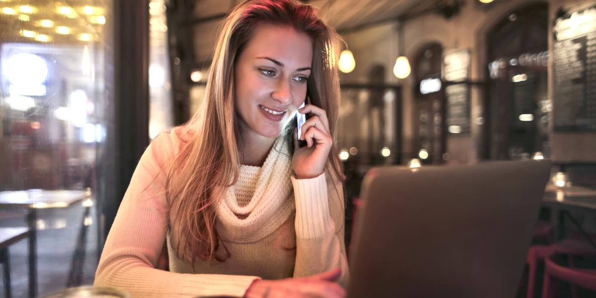Young happy woman on phone call while writing on laptop