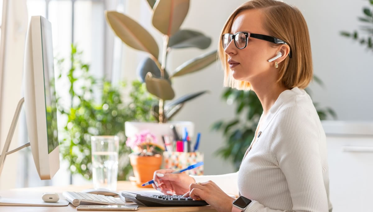 Woman sitting at desk using computer while wearing wireless headphones