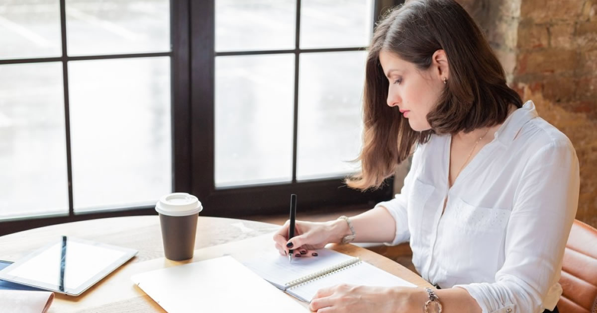 Businesswoman writing in notebook at table with coffee