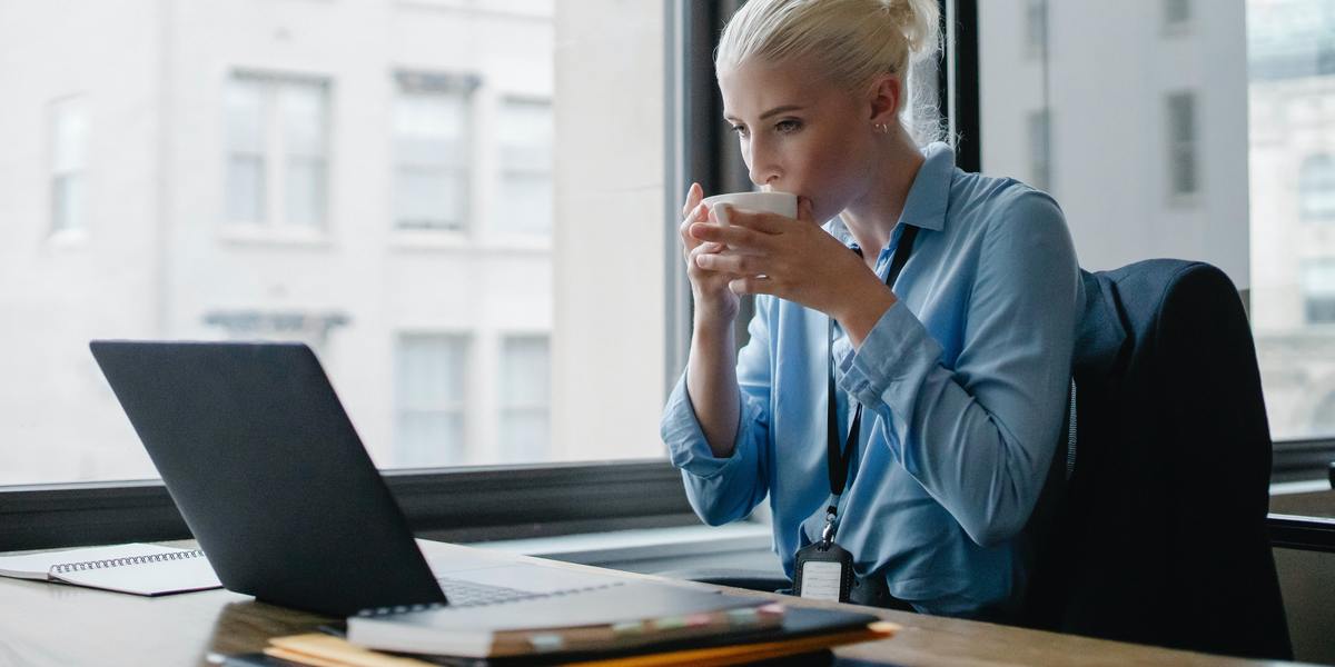 Jovem mulher de negócios tomando café e trabalhando no computador
