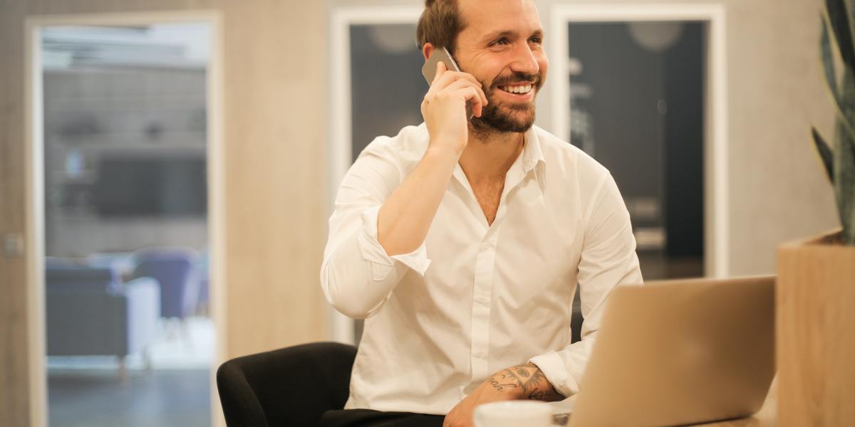 Escritor sorridente com laptop falando ao smartphone