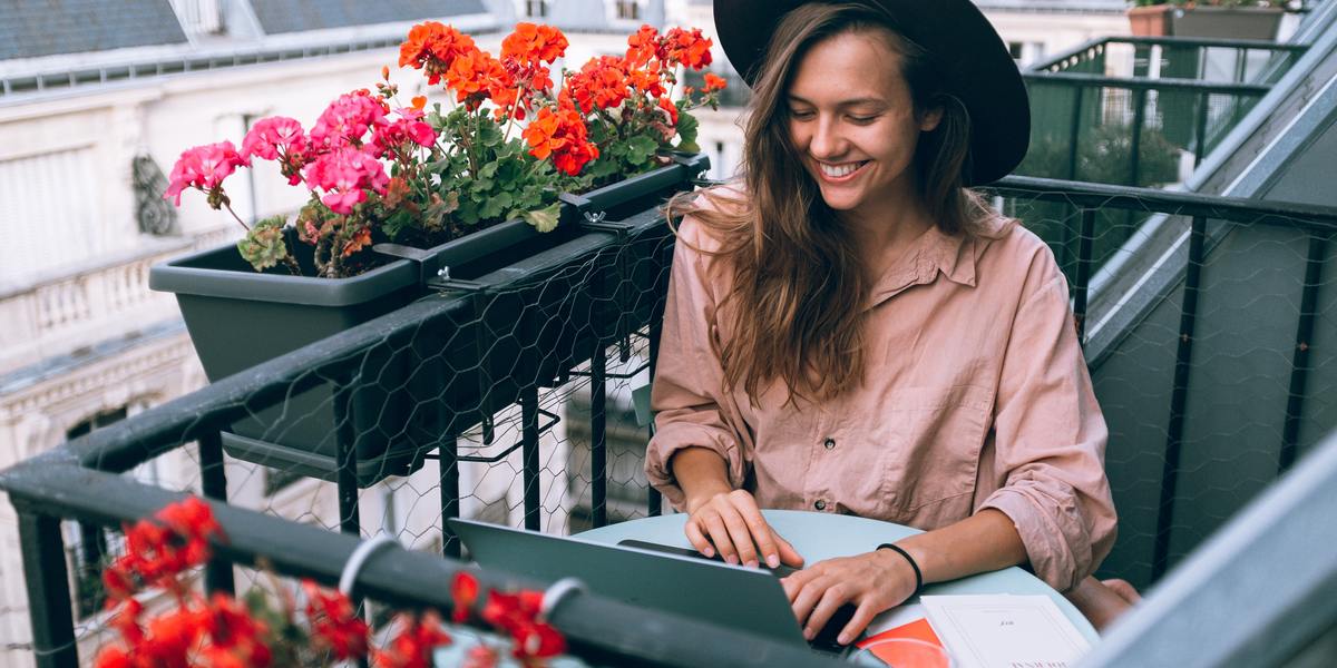 Young happy woman working on her laptop remotely on the balcony