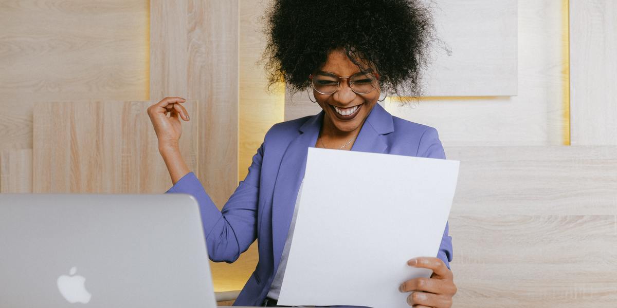 happy woman writer at her computer, holding a piece of paper