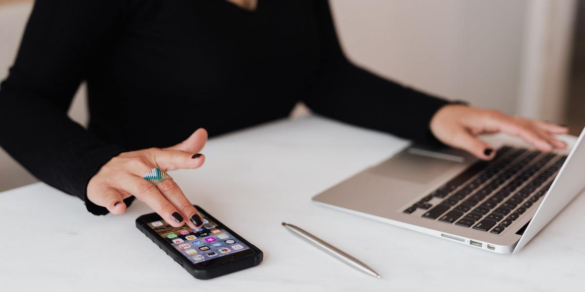 Social media manager looking at smartphone and laptop at desk