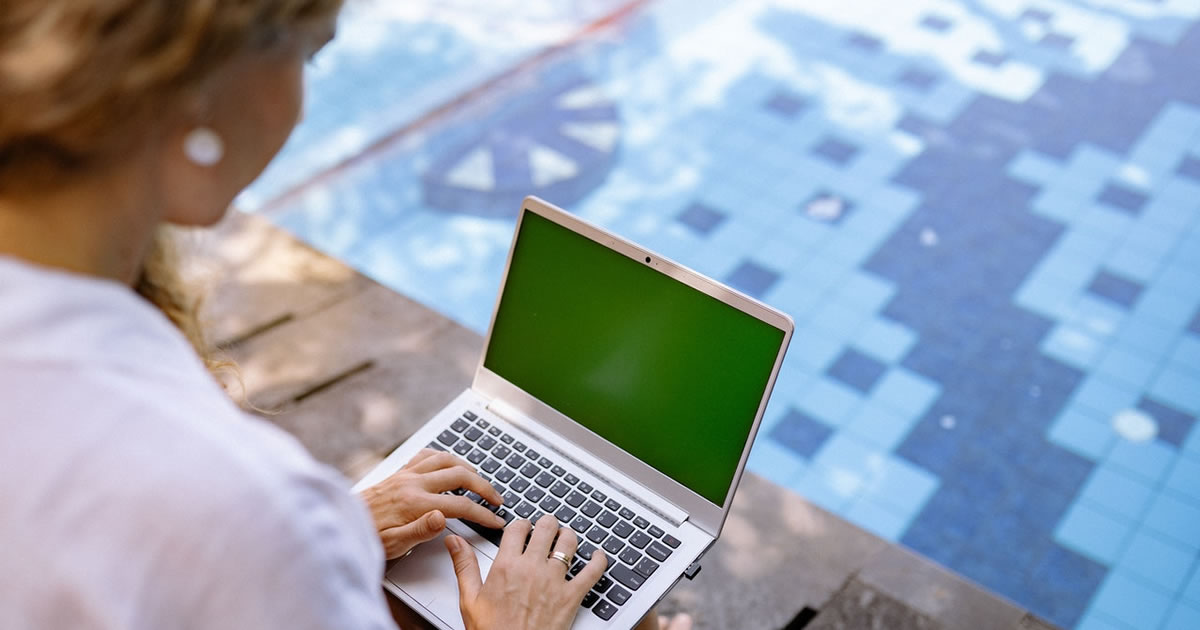 Mulher escrevendo em um laptop perto de uma piscina