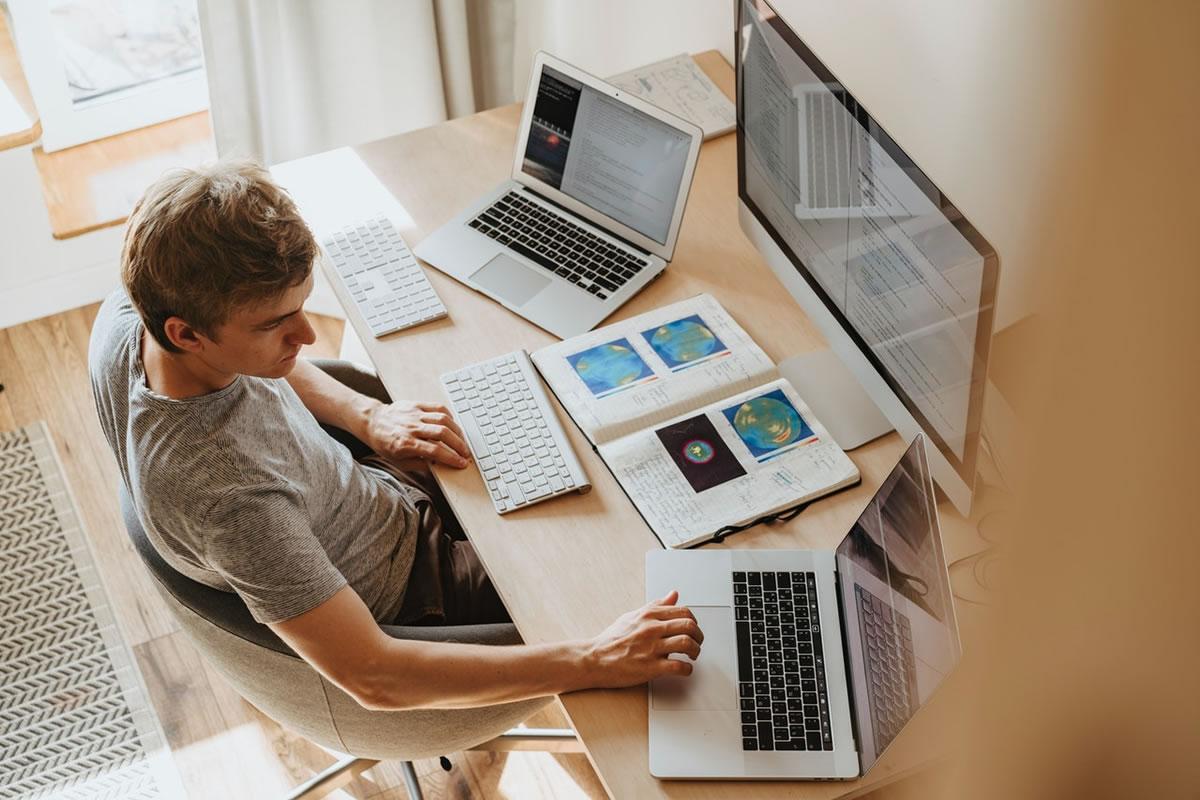 Homem em sua mesa trabalhando em 3 computadores