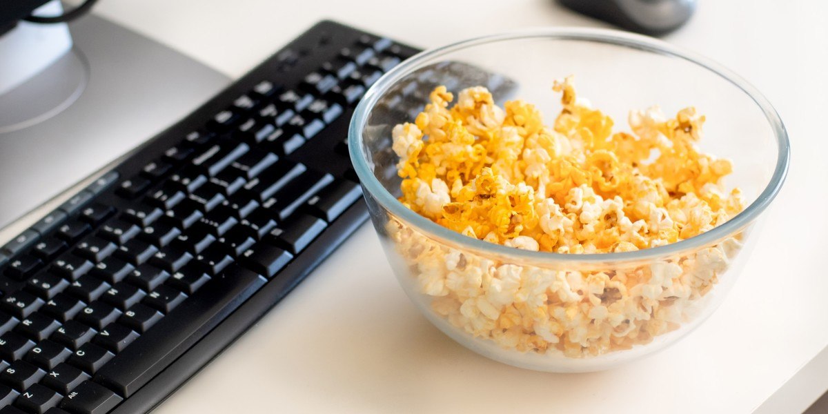 Bowl of popcorn on the table near the computer with keyboard and mouse.