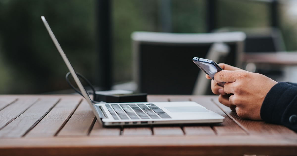 Man looking at smartphone and working on laptop