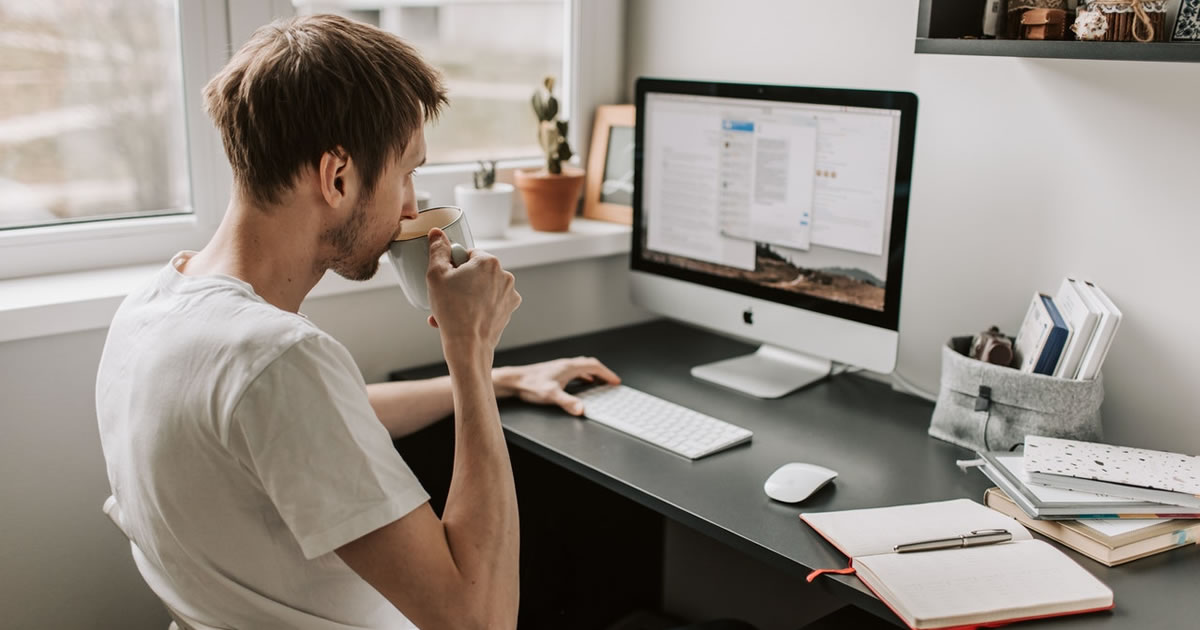 Man working on desktop computer, drinking from mug