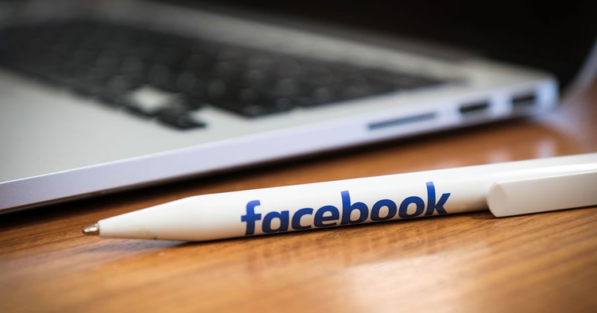 Closeup of a white pen with the word Facebook on it on a desk next to a laptop computer