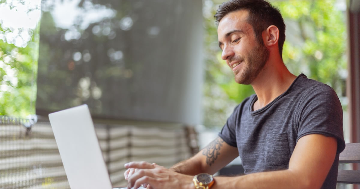 Smiling man writing on laptop at table