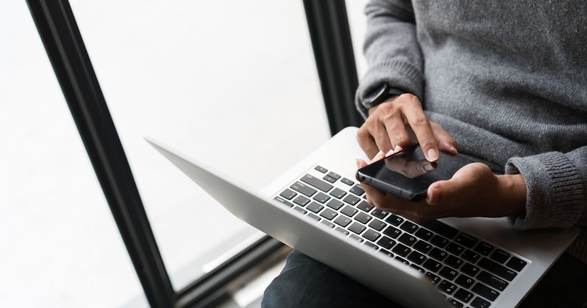 Writer browsing on smartphone with laptop on his lap