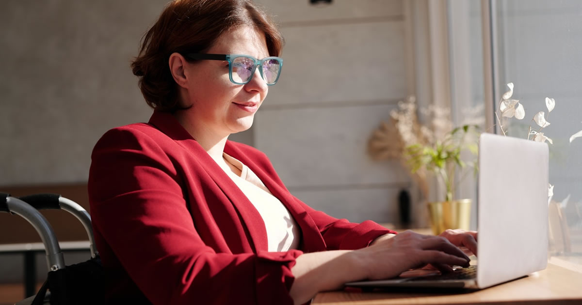 Woman in wheelchair writing on laptop at table