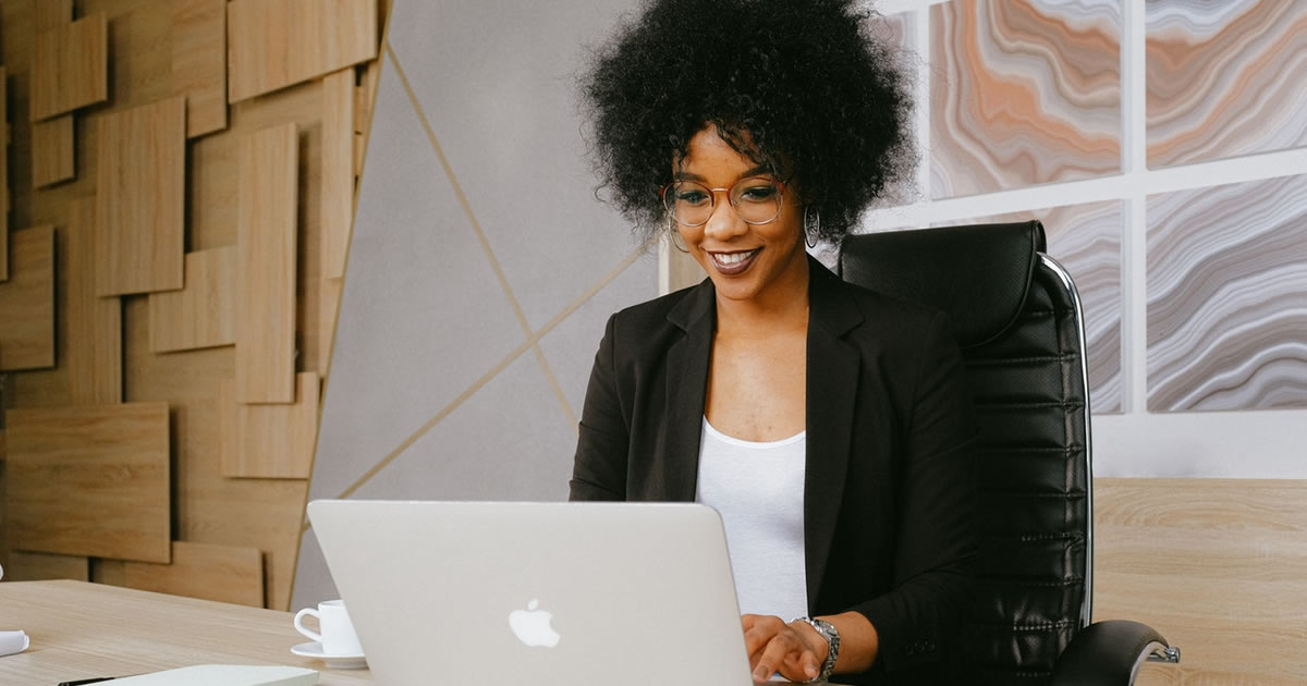 Smiling woman sitting at table writing on MacBook laptop