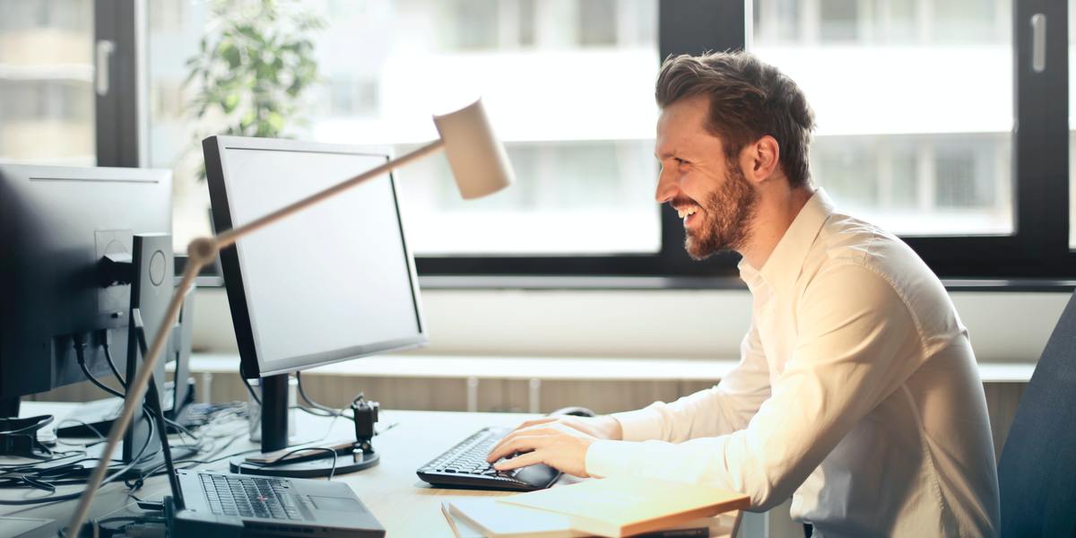 happy man writing on computer at desk